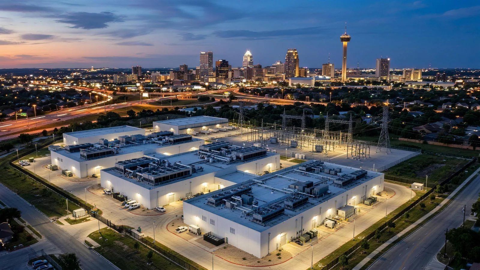 A data center campus at dusk with the San Antonio skyline and the Tower of the Americas behind it